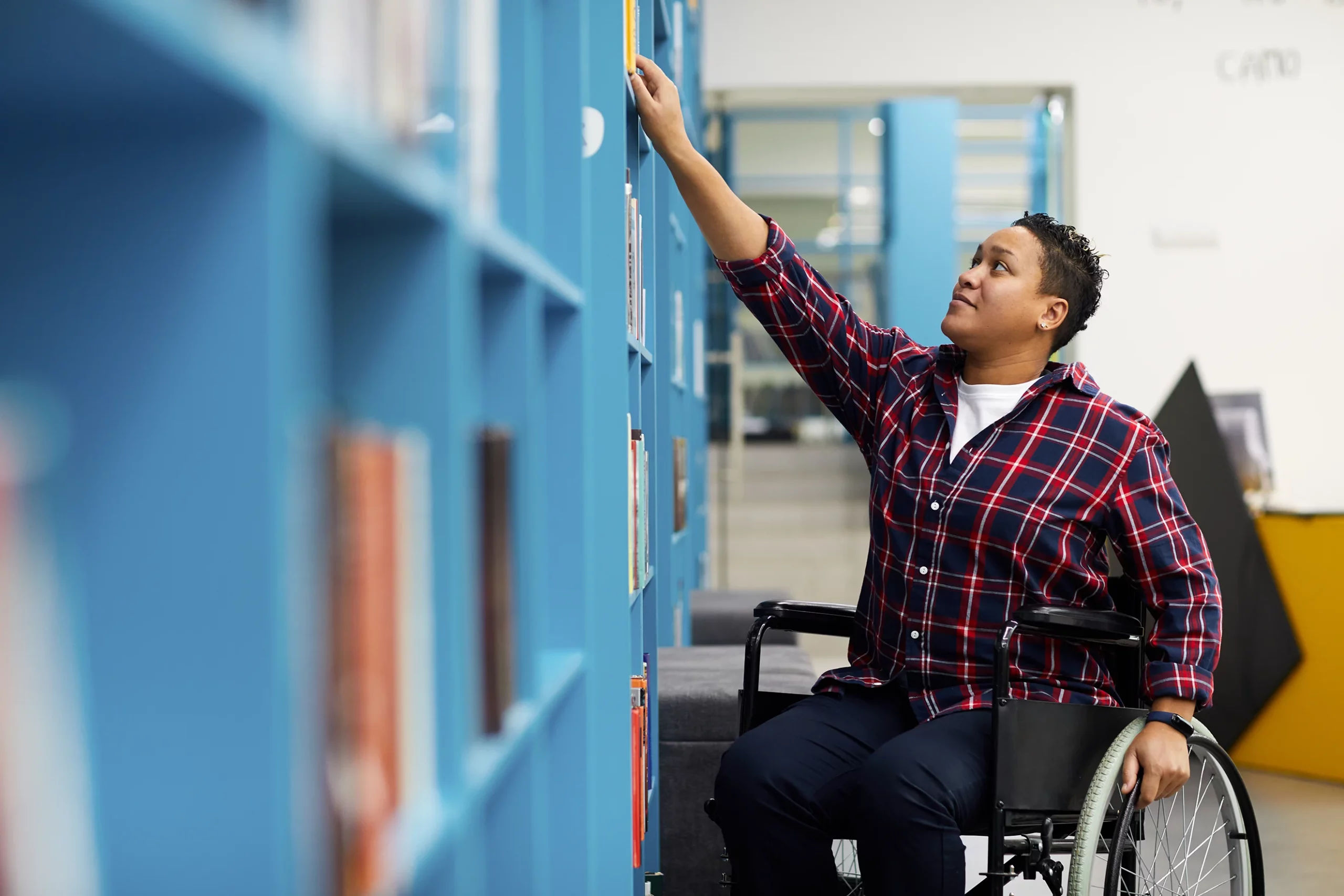 Person in a wheelchair reaching for a book on a shelf.